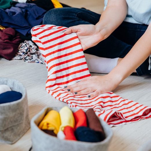 Woman tidying up wardrobe. Folding clothes and organizing stack of fresh laundry in boxes and baskets.